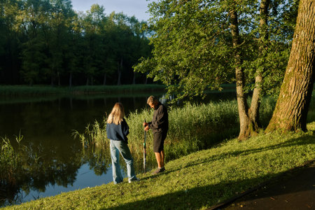 Man and woman are fishing peacefully by a lush pond, enjoying nature's beauty and tranquility.の写真素材