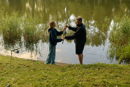 Man and woman smile while fishing together by a pond on a sunny day.の写真素材