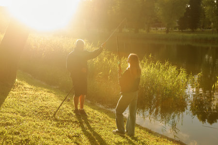 A man and a woman are fishing together by a calm pond, enjoying a warm, sunny day.の写真素材