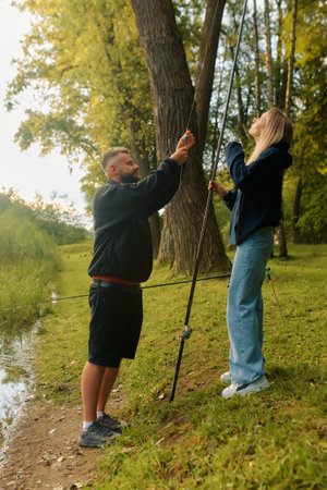 Man and woman set up fishing poles by a pond surrounded by lush greenery.の写真素材