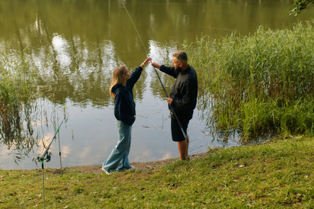 A man and woman share a moment fishing at a calm pond.の写真素材