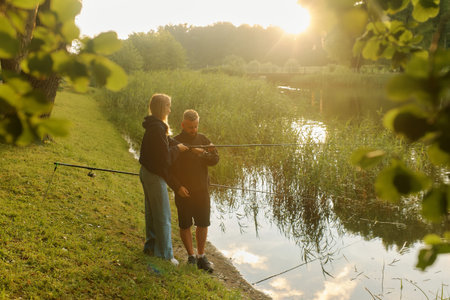 A man and a woman fish together by a pond at sunset, enjoying the warm glow.の写真素材