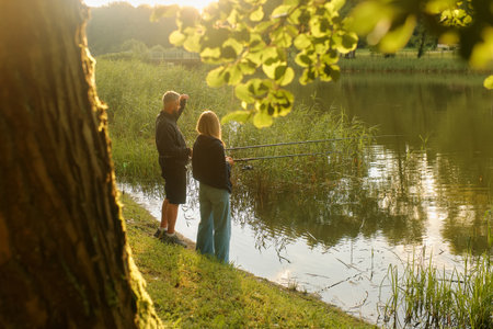 Man and woman stand side by side, fishing in a pond surrounded by nature.の写真素材