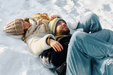 A couple lies together in untouched snow, embracing the peaceful winter atmosphere. They dress warmly and enjoy the quiet beauty of the snowy surroundings.の写真素材
