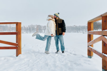 Winter couple shares a sweet moment on a snowy pier in a serene landscape.の写真素材