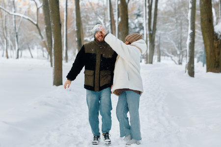 Two people walk hand in hand through a snow-covered park, laughing and playfully interacting as snowflakes fall around themの写真素材