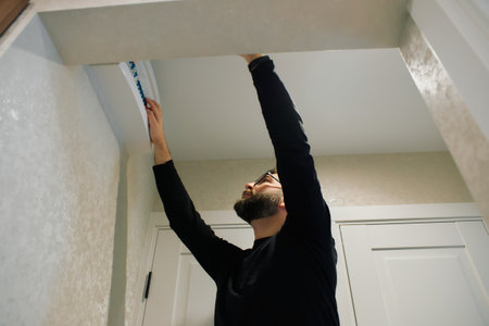 A man is focused on attaching trim above a doorway in a house.