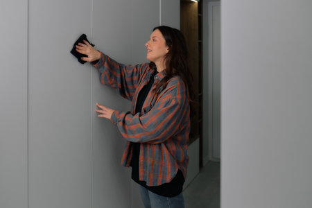 Woman is wiping a wall with a cloth in a home environment. She is smiling while she cleans.