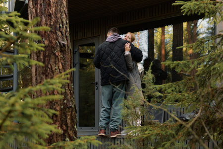 Couple shares a warm embrace on a wooden deck. Tall trees frame the scene, enhancing the tranquility of their intimate moment during autumn.の写真素材