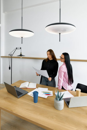 Women are engaged in a discussion while reviewing papers at a wooden table in a contemporary office.の写真素材