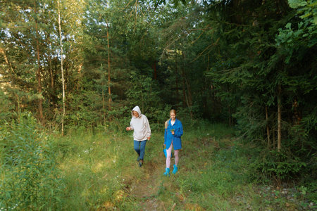 Two people stroll along a grassy trail in a forest. Sunlight filters through the trees while they explore the area together.の写真素材