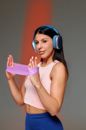 Woman is holding an exercise band in both hands while wearing headphones. She focuses on her workout...