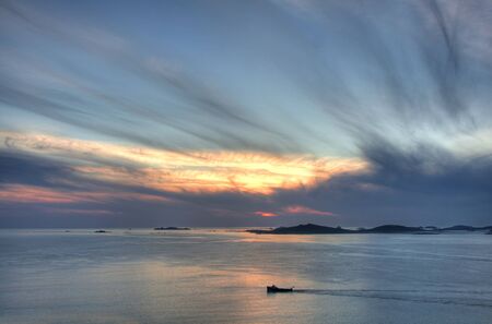 Lone boat passing Samson island at sunset from St Maryâ€™s, Isles of Scilly, Cornwall, England.
