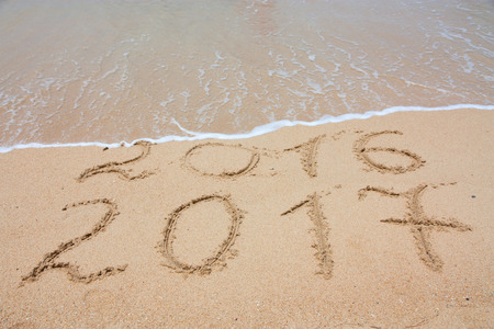 New Year 2017 is coming concept - inscription 2017 and 2016 on a beach sand, the wave is covering...