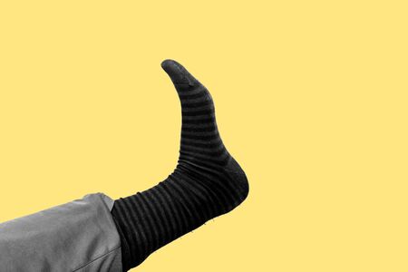 Contemporary art collage. Leg of a man that shows a long striped cotton sock in black and white with a yellow backgroundの写真素材