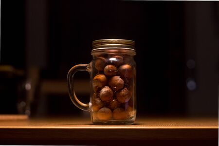 Mason jar with a bunch of brown nuts on a wooden table with a dramatic light with a dark blurred...