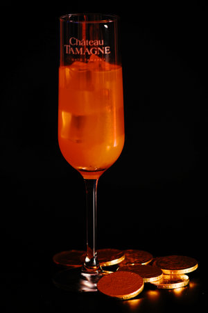 A glass of orange cocktail with gold coins on a black background.の写真素材