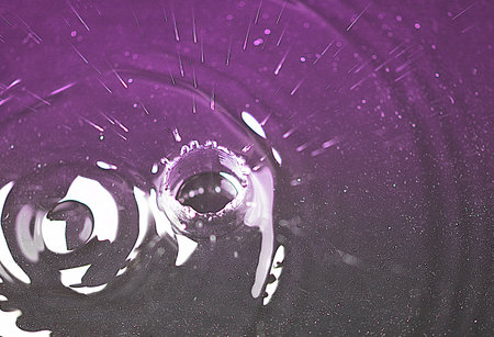 Water drop with ripples and splashes on a purple background.の写真素材