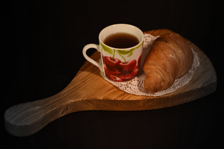Cup of coffee and croissant on wooden board on black backgroundの写真素材