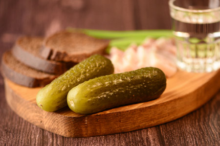 pickled cucumbers on a wooden board and a glass of vodkaの写真素材