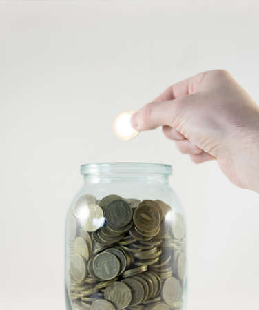 Glass jar with money on a white background. Hand with a coinの写真素材