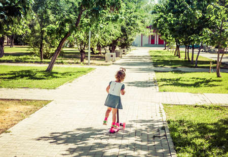 Cute child skilfully skates on a pink two-wheeled scooter on a summer sunny dayの写真素材