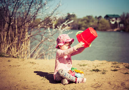 Cute baby girl playing in the sand with a red bucketの写真素材