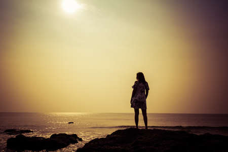 Silhouette of a young woman against the background of the sea and the sun