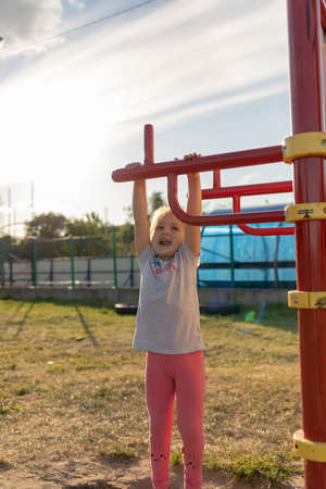 A small child goes in for sports in the stadium. hanging on the horizontal bar, on the uneven bars