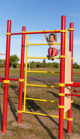 A small child goes in for sports in the stadium. hanging on the horizontal bar, on the uneven barsの写真素材