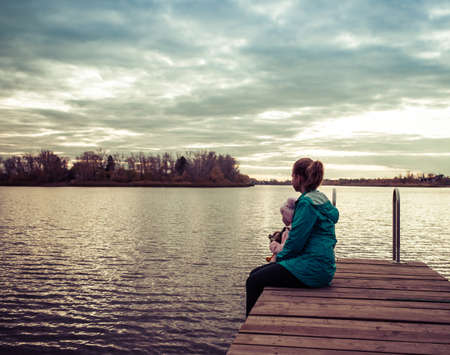 mom and daughter are sitting on the pier at sunsetの写真素材