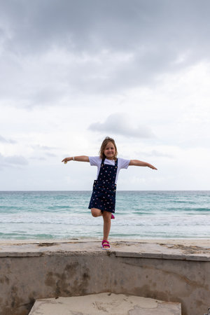 the child stands on one leg, arms outstretched to the sides against the background of the seaの写真素材