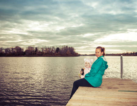 mom and daughter are sitting on the pier at sunsetの写真素材
