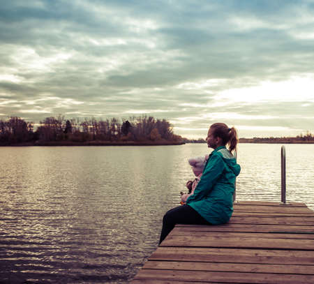 mom and daughter are sitting on the pier at sunsetの写真素材