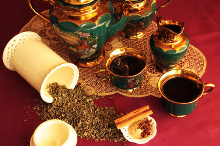still life with green golden tea set loose tea sweets and flavoring on a burgundy backgroundの写真素材