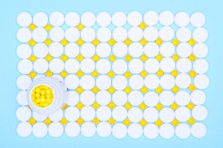 Background of white and yellow pills and a jar of yellow pills.Various medications: pills, blister pills, drugs, macros, copy space on a blue background.の写真素材