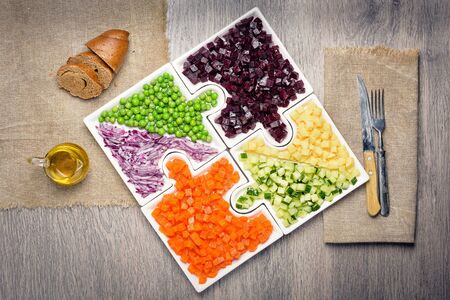 
Raw vegetables carrots, peas, onions, cucumber, potatoes, beets cut into cubes lie on puzzles in the form of puzzles and gather in a single large dish.の写真素材