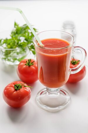 Tomato juice is poured into a transparent glass with parsley and herring, on a white background with cherry tomatoes, lit by sunlightの写真素材