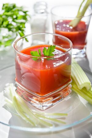 Tomato juice is poured into a transparent glass with parsley and herring, on a white background, illuminated by sunlight.の写真素材