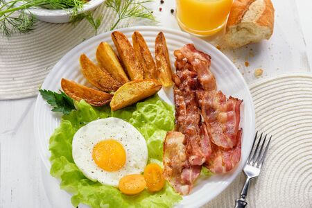 
French fries and egg with bacon on top in a white bowl, on a large table with greens.の写真素材