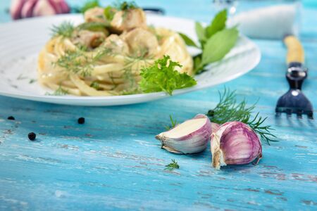 A dish standing on a blue wooden table, a plate with Italian pasta and a chicken with a sauce of Provencal herbs, decorated with greens, salt and garlic, close-up.の写真素材