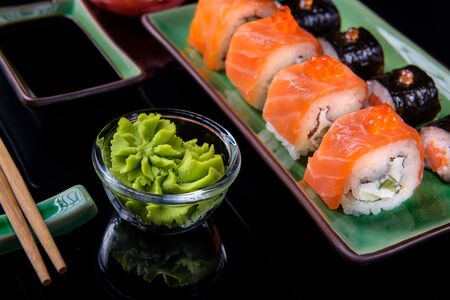 Japanese food. A set of various rolls of salmon, eel, shrimp and red caviar, in a beautiful green bowl, on a black background with reflection.の写真素材