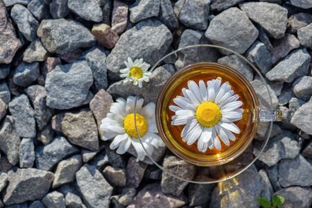 A cup of tea with a white chamomile, close-up, lit by a warm sunlight, standing on granite stonesの写真素材
