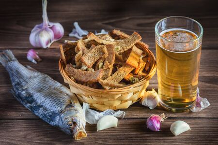 Home snack for beer as rye crisps with garlic, lying in a wooden table in the rays of sunlight, next to it there is a glass with freshly poured beer.の写真素材