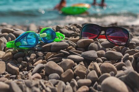 Beach vacation by the sea on a pebble beach. Ochki blue-green for swimming and red sun-lying on the...