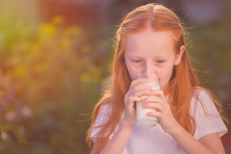 Portrait of a beautiful redhead girl drinking fresh milk outdoors.の写真素材