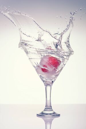 Frozen splashes of clean, spring water, in a glass with frozen strawberries, on a white background.の写真素材