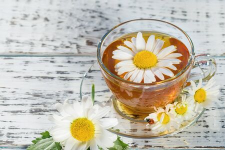 A cup of tea standing on a wooden, white table, in the flowers of the daisy field, to which the ladybug flew.の写真素材