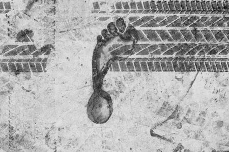 Background texture of a trace of feet and tires on the asphalt. Close-up. Texture design of car tires and a footprint of a person. A trace of a man's foot on black asphalt and car tires.の写真素材