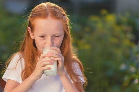 Portrait of beautiful redhead girl drinking fresh milk outdoors.の写真素材